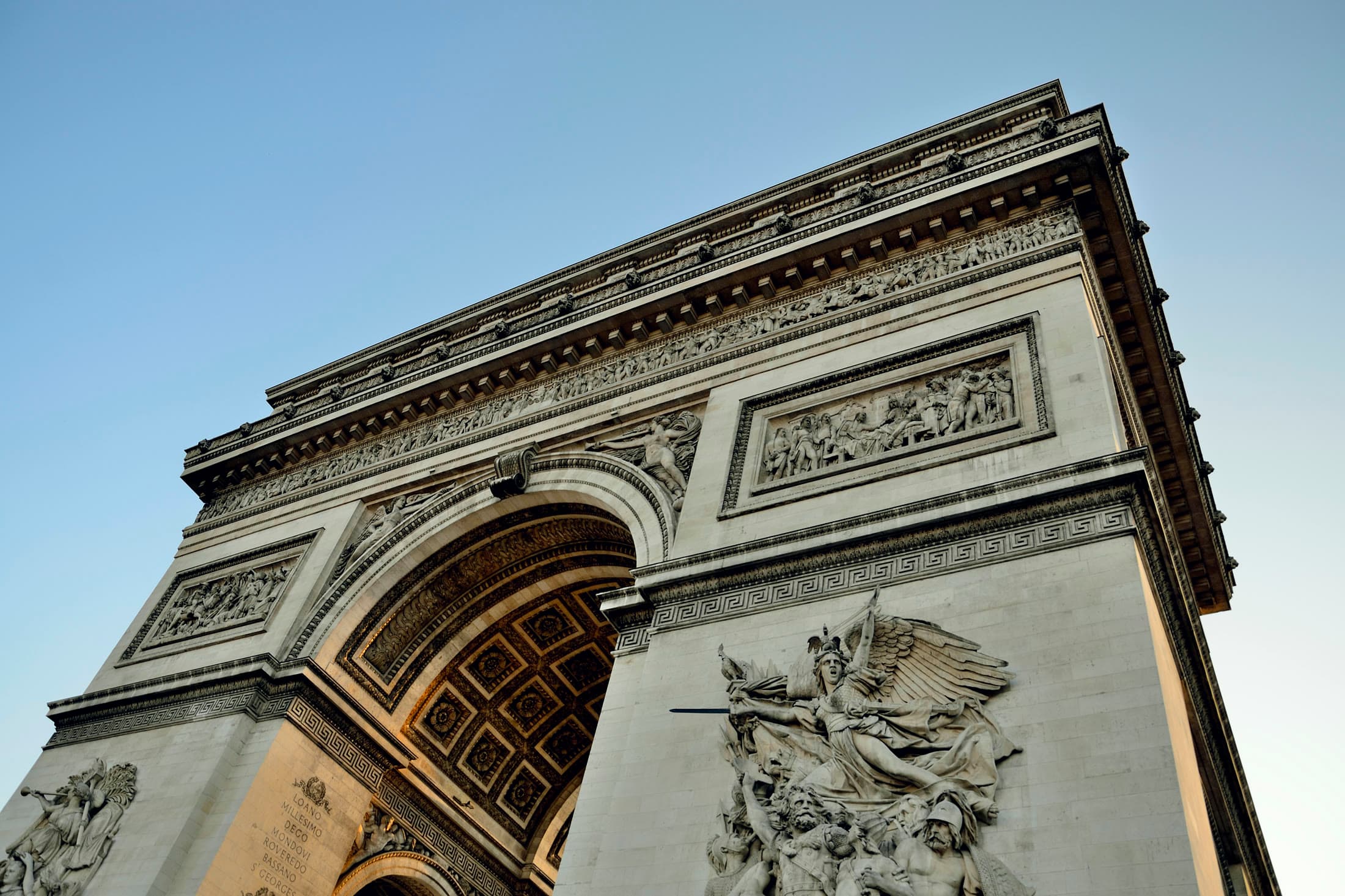 Low-angle view of the Arc de Triomphe against a clear Paris sky.